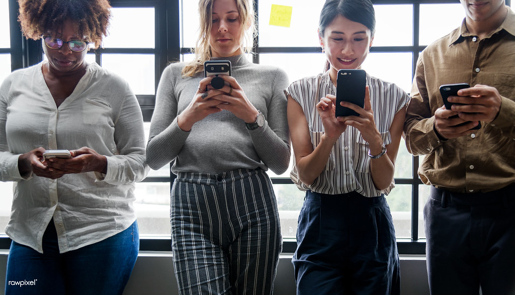Four young adults standing by a window looking at their smartphones